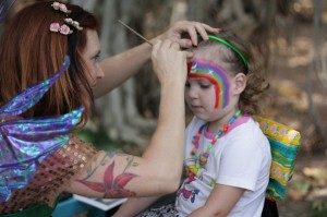 lara face painting a rainbow on a girl in the park